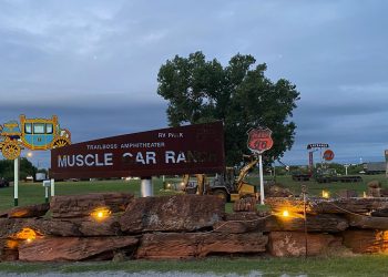 Muscle Car Ranch owner Curtis Hart and Ranch Hand Randy work to install a Phillips 66 sign just before dusk Wednesday evening. The orange and black sign replaces a red and white Phillips 66 sign that was dislodged during a 2013 tornado that hit Chickasha, Hart said. The replacement sign came down as hurricane Camile made landfall in Corpus Christi in 1969. Featuring chart-topping artists and bands from several genres, Hart’s Muscle Car Ranch has held concerts since 1992. Photo by Curtis Awbrey