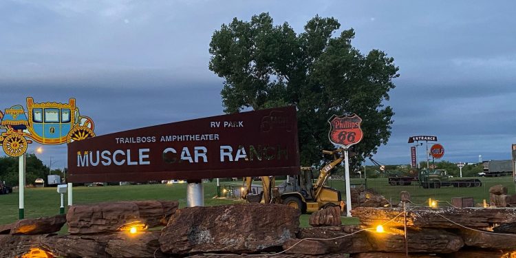 Muscle Car Ranch owner Curtis Hart and Ranch Hand Randy work to install a Phillips 66 sign just before dusk Wednesday evening. The orange and black sign replaces a red and white Phillips 66 sign that was dislodged during a 2013 tornado that hit Chickasha, Hart said. The replacement sign came down as hurricane Camile made landfall in Corpus Christi in 1969. Featuring chart-topping artists and bands from several genres, Hart’s Muscle Car Ranch has held concerts since 1992. Photo by Curtis Awbrey