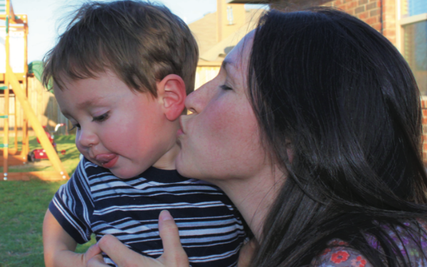 A mom cuddles up close to steal a kiss from her toddler