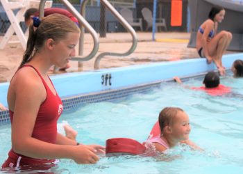 Rachel Gregg, high school lifeguard, watches as Brynlee Sanders of Cyril, age 4, uses a flotation device to swim the width of the pool