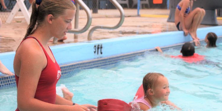 Rachel Gregg, high school lifeguard, watches as Brynlee Sanders of Cyril, age 4, uses a flotation device to swim the width of the pool